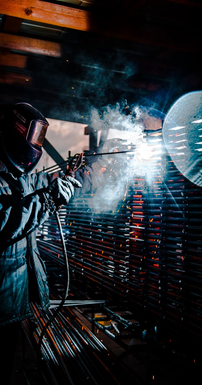 A welder in protective gear working with bright sparks and smoke in an industrial setting.