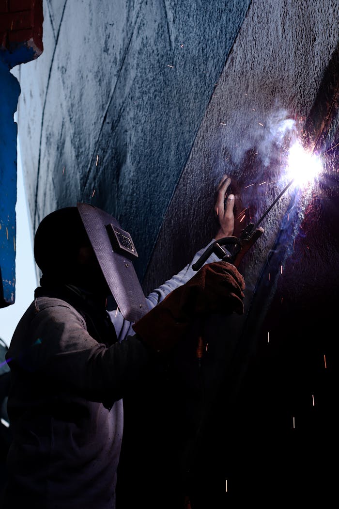 A skilled welder works on a metal surface, creating bright sparks in an indoor setting.