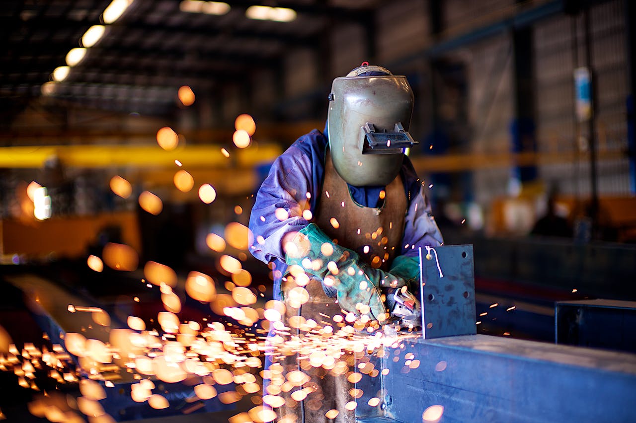 An industrial worker in a workshop welding metal with protective gear, creating vibrant sparks.